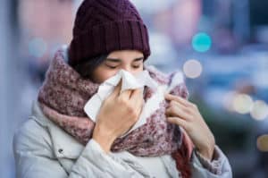 Pretty young woman blowing her nose with a tissue outdoor in winter. Young woman getting sick with flu in a winter day. Woman with a cold.