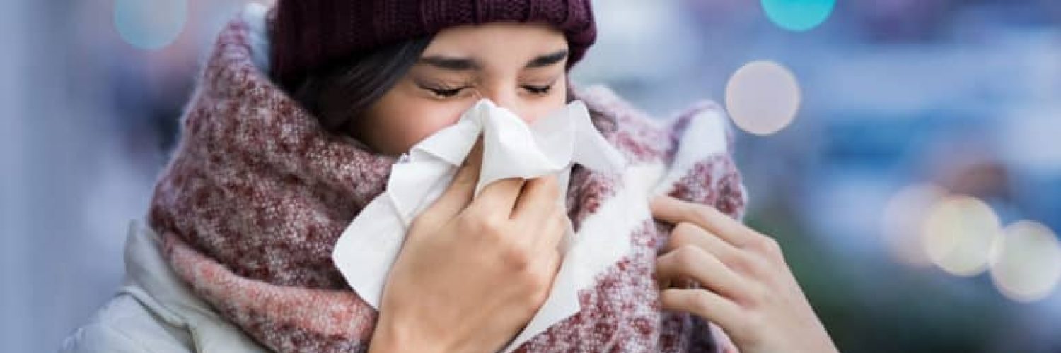 Pretty young woman blowing her nose with a tissue outdoor in winter. Young woman getting sick with flu in a winter day. Woman with a cold.