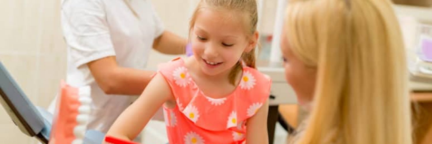 Dentist learning little girl patients how to brush her teeth with toothbrush. Selective focus. Focus on little girl.