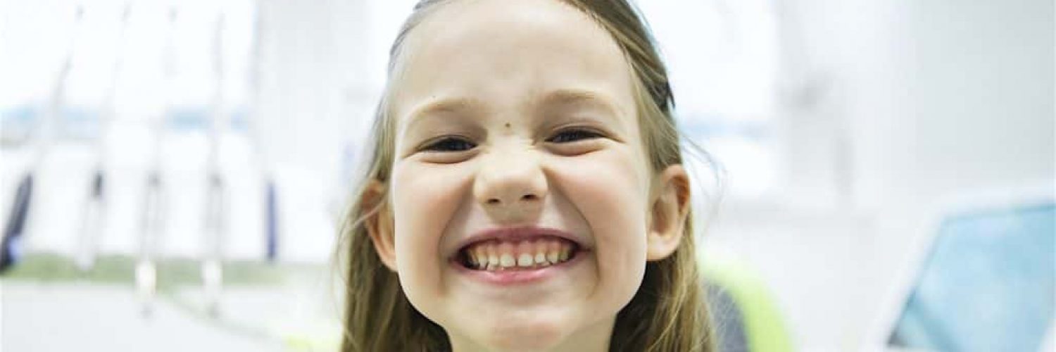 Girl showing her healthy milk teeth at dental office