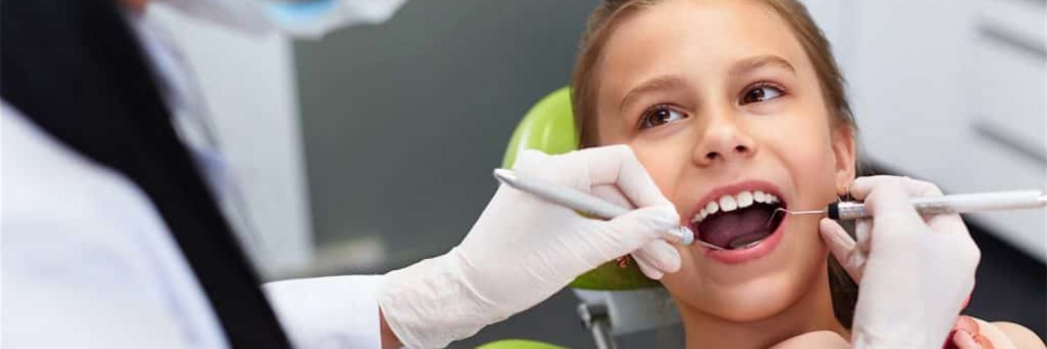 Teeth checkup at dentist's office. Dentist examining girls teeth in the dentists chair